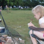 Girl with a hot chocolate dipper treat sitting around the campfire