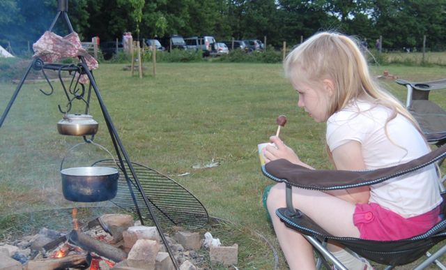 Girl with a hot chocolate dipper treat sitting around the campfire