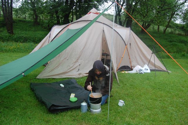 Cath cooks under the tarp while wearing a buff against the midges